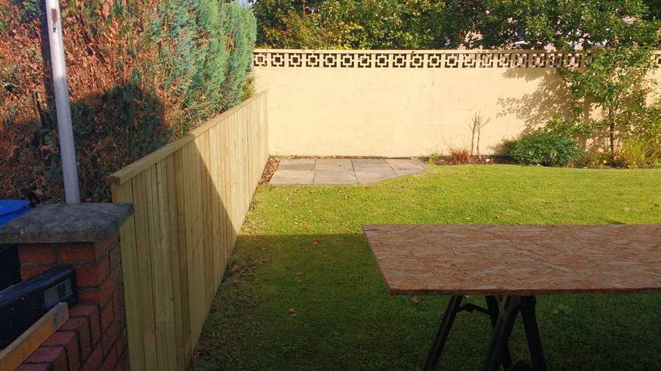 A new close-board fence along a lawn beside a rendered wall